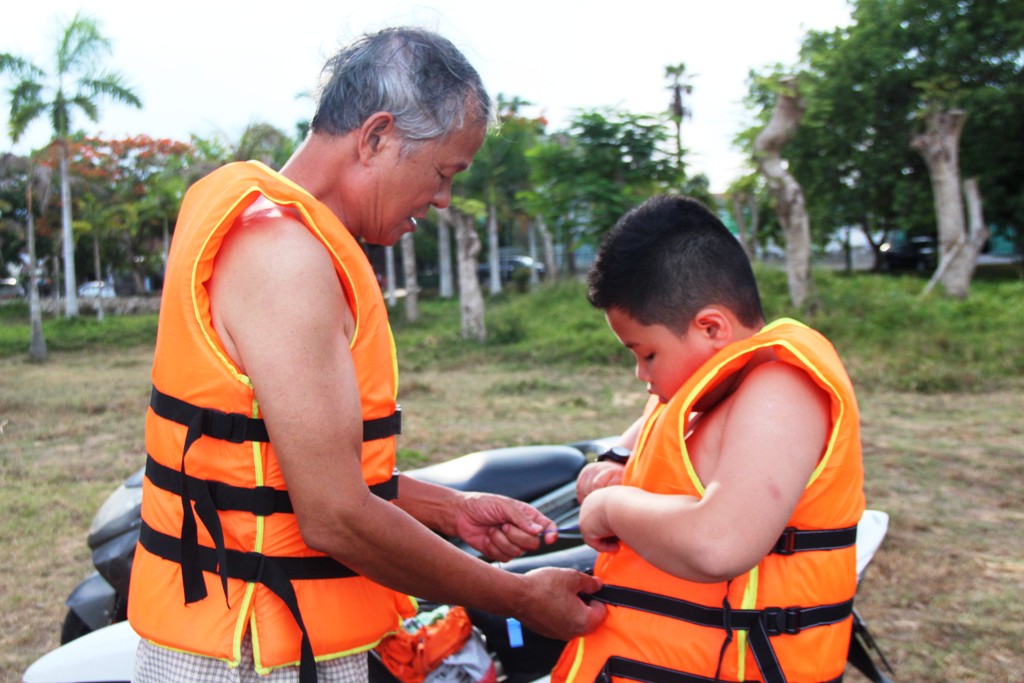 The old man wearing a life jacket for his grandchildren before joining into the cool water