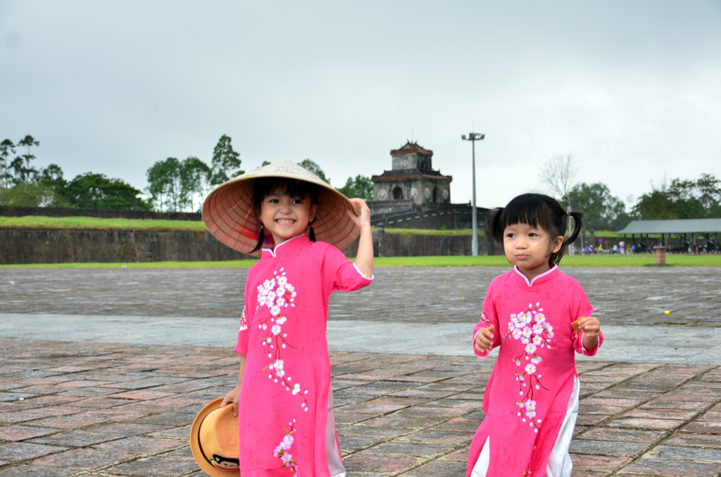 Two child tourists in Ao Dai and conical hats are exploring Hue